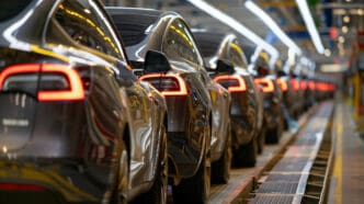 New black electric cars with illuminated tail lights line up on an automotive production floor.