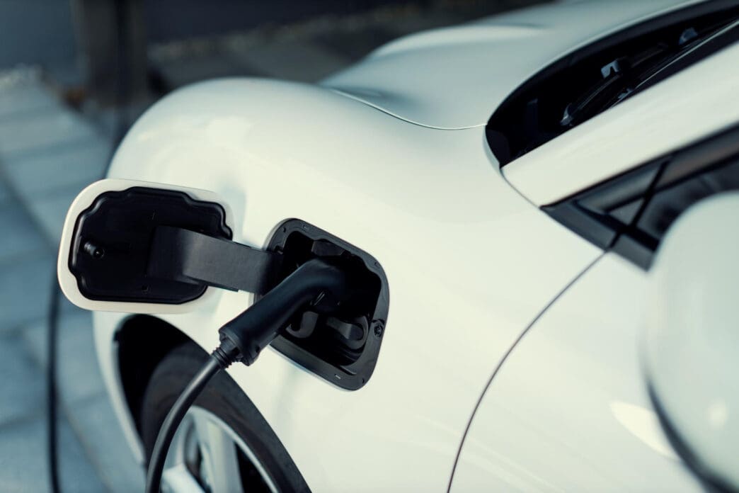 Close-up view of a black charging cable plugged into the charging port of a white electric vehicle.