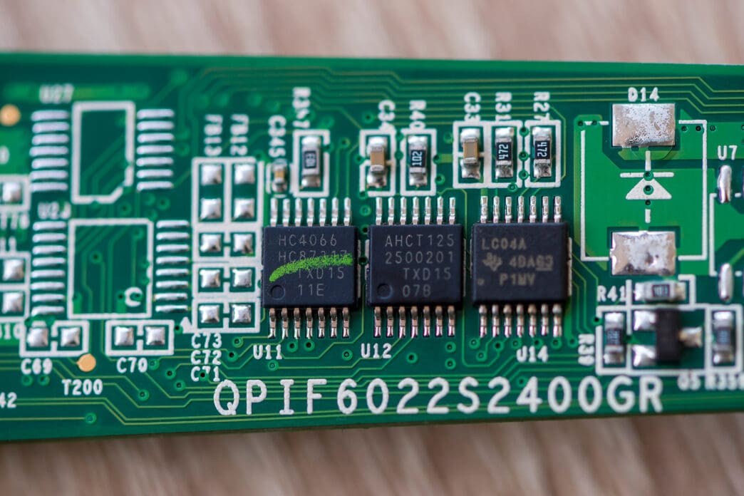 A macro photo of a green circuit board showing Nexperia HC4066, Jabbar AHCT125, and TI LC04A microchips.