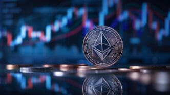 A physical silver Ethereum coin stands on a reflective surface, with a blurry blue and red financial market chart in the background.