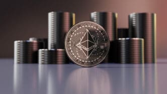 A silver Ethereum (ETH) coin standing in front of several dark coin stacks.
