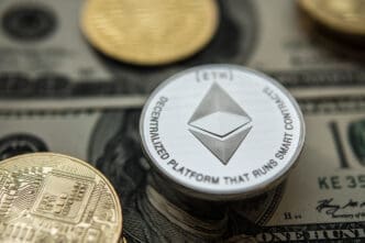 A silver Ethereum coin on top of a US one-hundred-dollar bill with other crypto coins nearby.