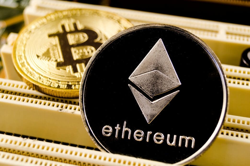 Physical silver Ethereum and gold Bitcoin coins resting on computer hardware.