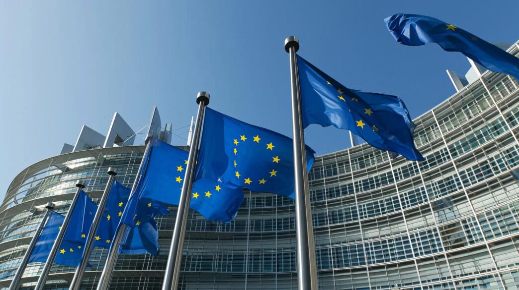 A row of European Union flags waving in front of the European Parliament building.