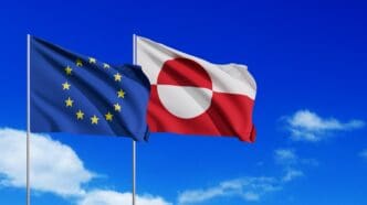 The EU and Greenland flags waving against a bright blue sky with clouds