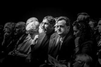 Black and white photo of a serious audience at a conference, focusing on two men in the foreground.