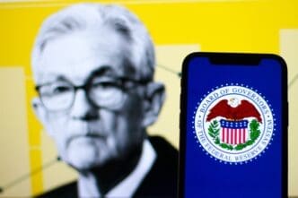 The Federal Reserve logo on a smartphone, with Fed Chair Jerome Powell in the background.