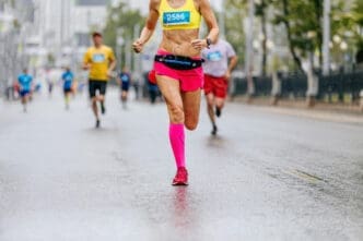 Female marathon runner in a yellow top and bright pink shorts and compression socks running on a wet city street.