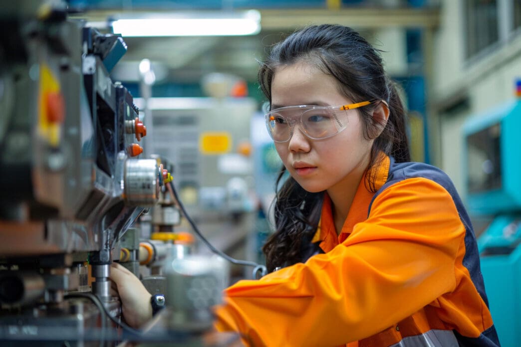 Young female engineer wearing safety glasses works on machinery