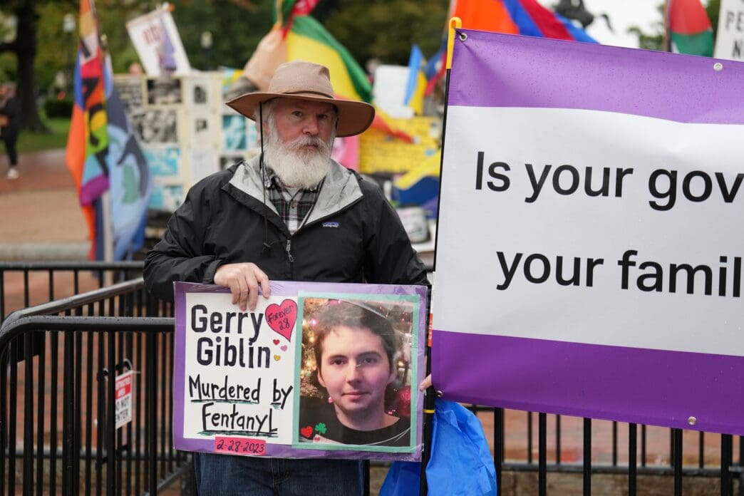 Man with a beard and a hat holding a sign for his son, Gerry Giblin, who died from Fentanyl.