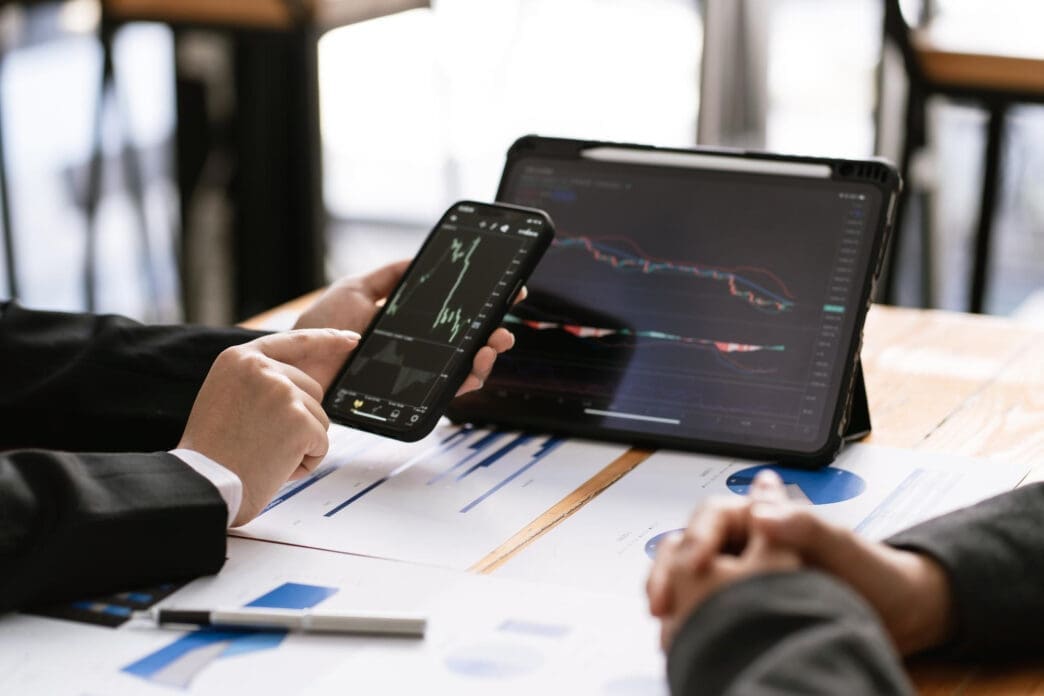 Two people analyzing financial charts on a smartphone and tablet during a meeting.