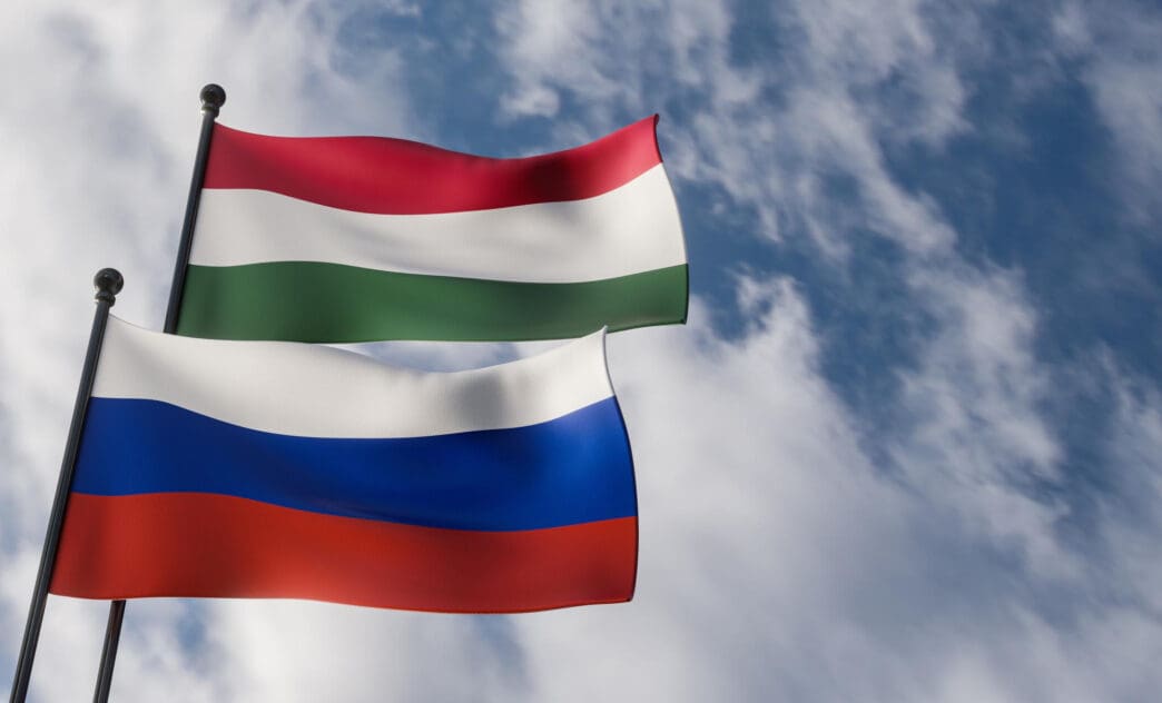 Hungarian and Russian flags waving on poles against a blue sky