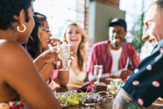 A diverse group of friends laughing and celebrating at a sunny indoor table with drinks and party streamers.