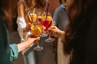 A group of people toasting together with colorful spritz cocktails in wine glasses.