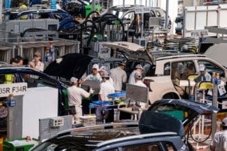 Workers in uniforms assemble electric cars on a busy factory production line.