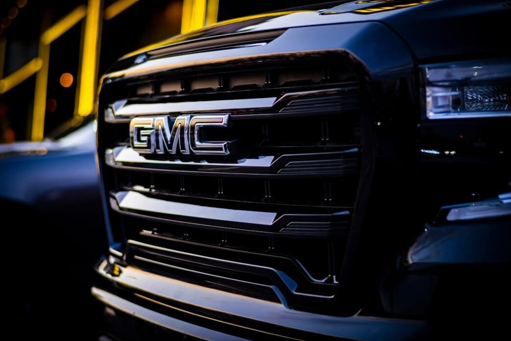 A close-up of the large, chrome GMC logo on the black front grille of a Denali Sierra pickup truck.