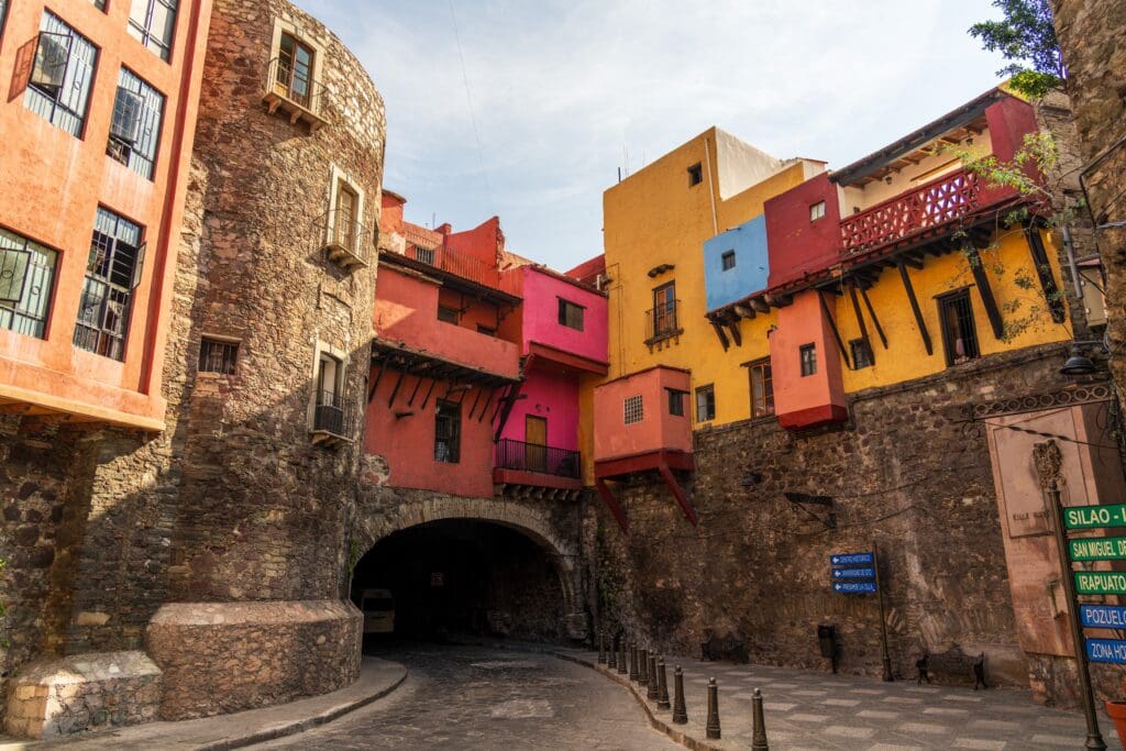 Historic tunnel entrance in Guanajuato, Mexico, framed by towering, colorful colonial houses built directly onto the stone wall.
