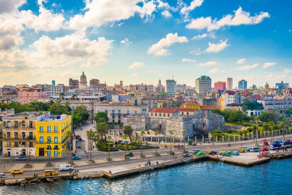 Wide, elevated view of the Havana, Cuba, downtown skyline and waterfront, featuring historic forts and colorful buildings along the Malecón.