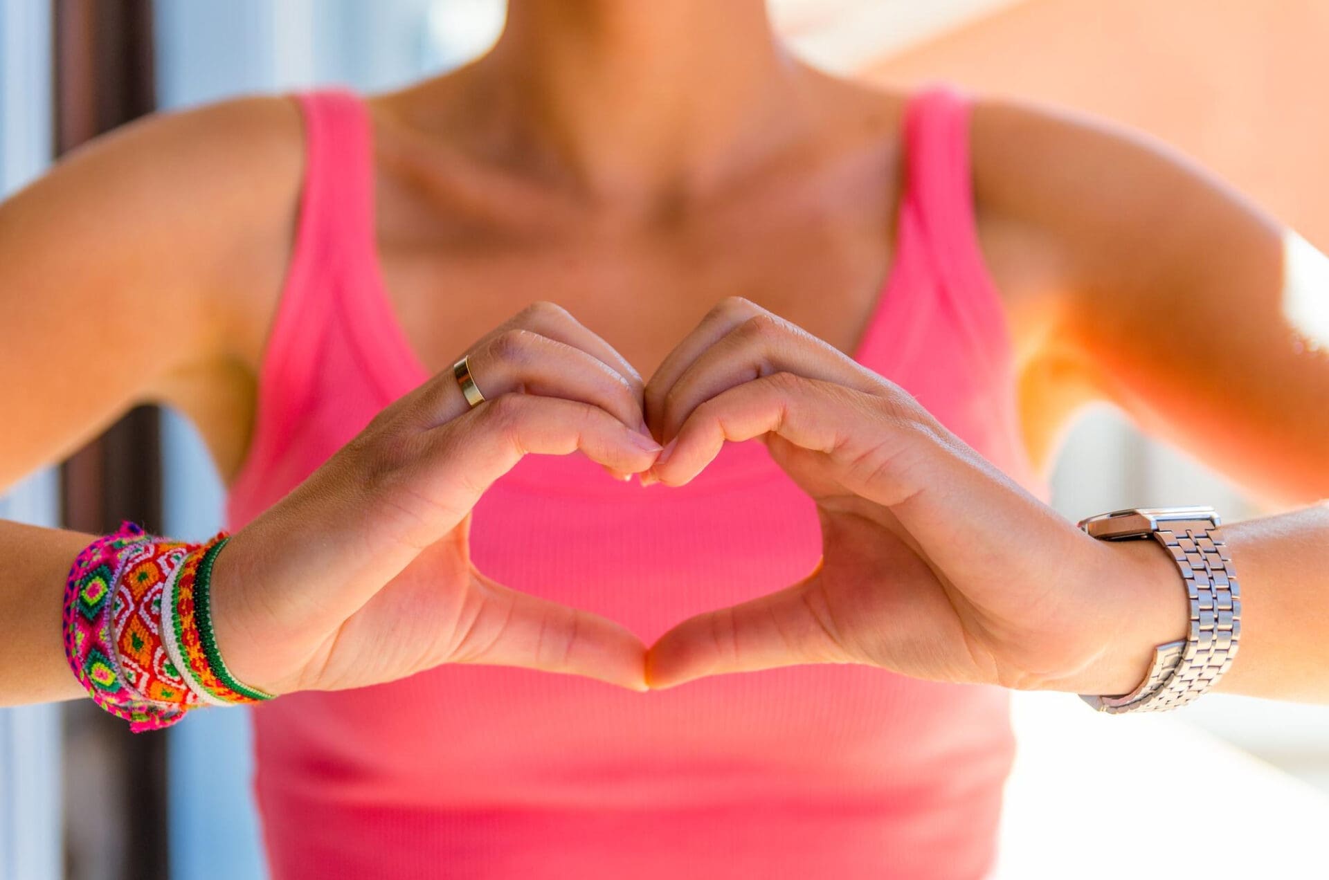 Woman forms a heart shape with her hands, wearing bracelets and a ring