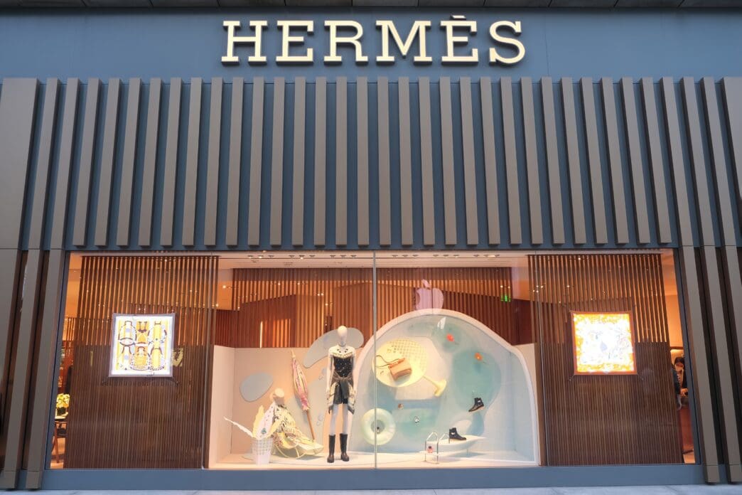 The storefront of a modern Hermès luxury fashion store in Shanghai, featuring a creative window display with mannequins.