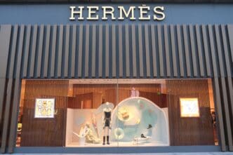 The storefront of a modern Hermès luxury fashion store in Shanghai, featuring a creative window display with mannequins.