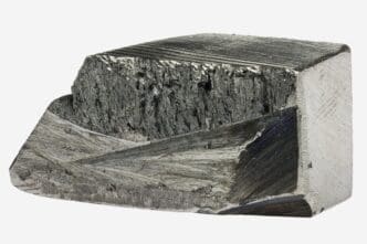 Irregular, cuboid chunk of dark gray metallic dysprosium showing a combination of rough, crystalline, and smoothly machined surfaces.