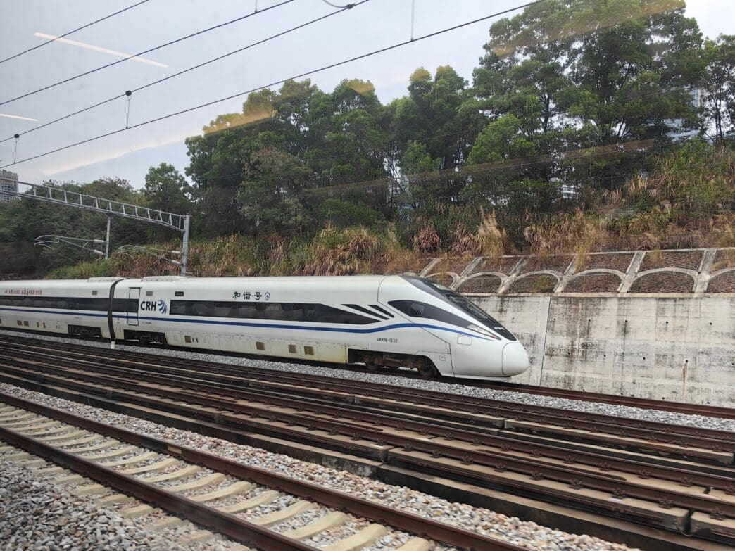 A white CRH1E high-speed train slows down on tracks with greenery and a retaining wall in the background