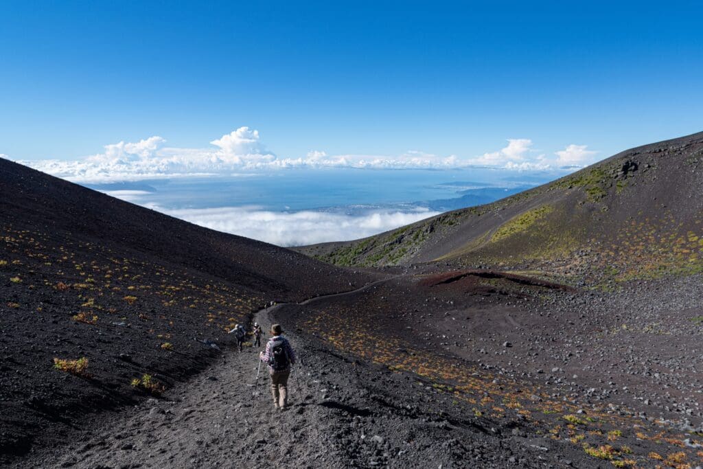 Hikers walk along a volcanic trail on Mount Fuji, descending towards Hoei No. 1 Crater.