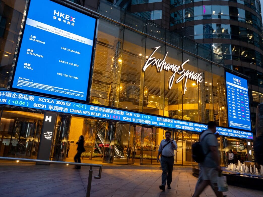 The illuminated facade of Exchange Square in Hong Kong at night, featuring stock market screens and a large "Exchange Square" sign.