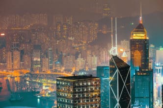 A sprawling cityscape at night, with illuminated skyscrapers, a harbor, and a hazy, glowing background