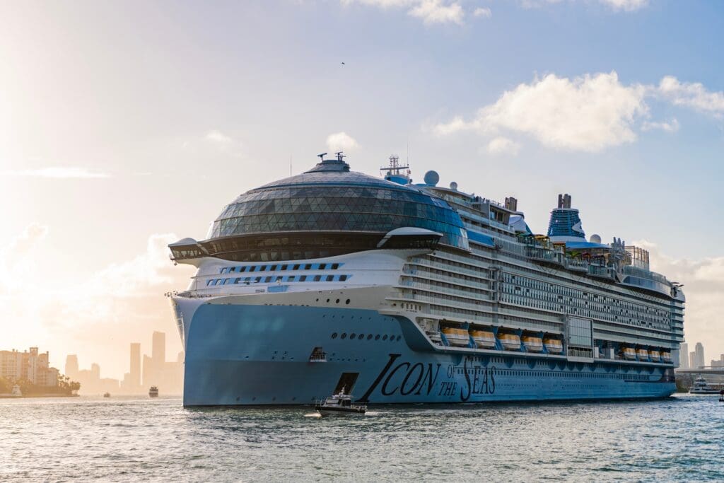 The massive Royal Caribbean cruise ship, Icon of the Seas, sails from the Port of Miami with the city skyline in the background.
