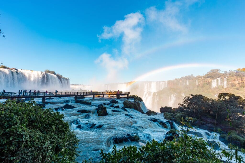 A beautiful view of Iguazu Falls with a rainbow over the mist and tourists on a walkway.