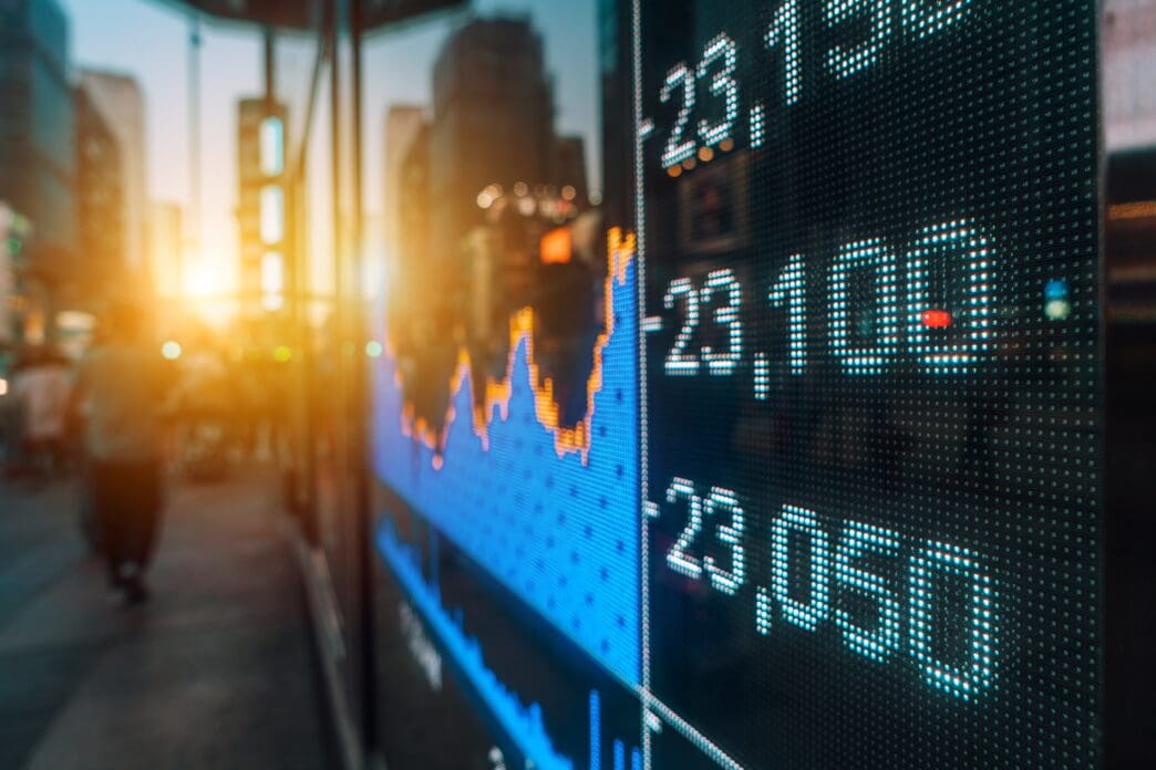 A close-up of a digital stock market graph on a city street at sunset.