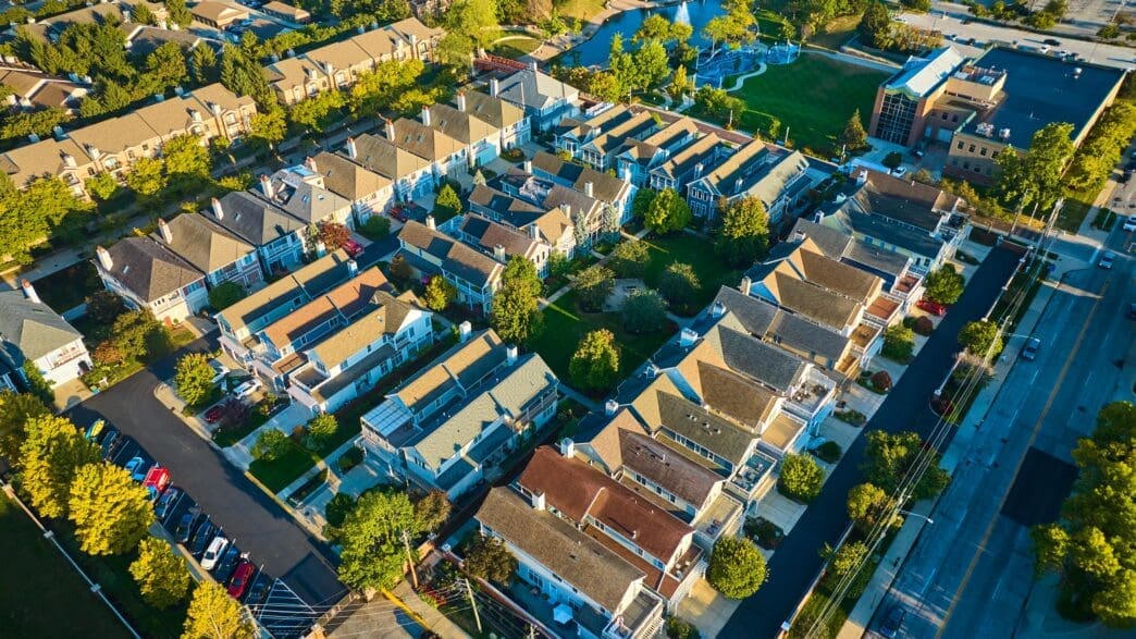 Aerial view of a dense, planned suburban neighborhood with uniform houses and green space at sunset.