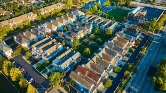 Aerial view of a dense, planned suburban neighborhood with uniform houses and green space at sunset.