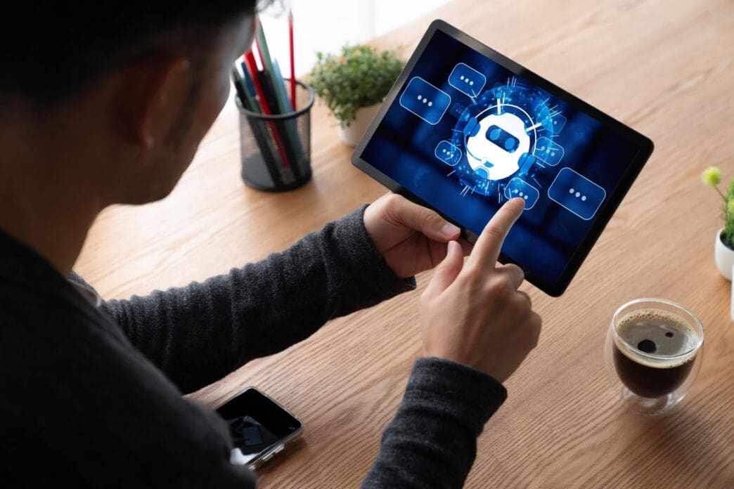 Person interacts with a digital tablet displaying a chatbot interface with a robotic head icon and speech bubbles
