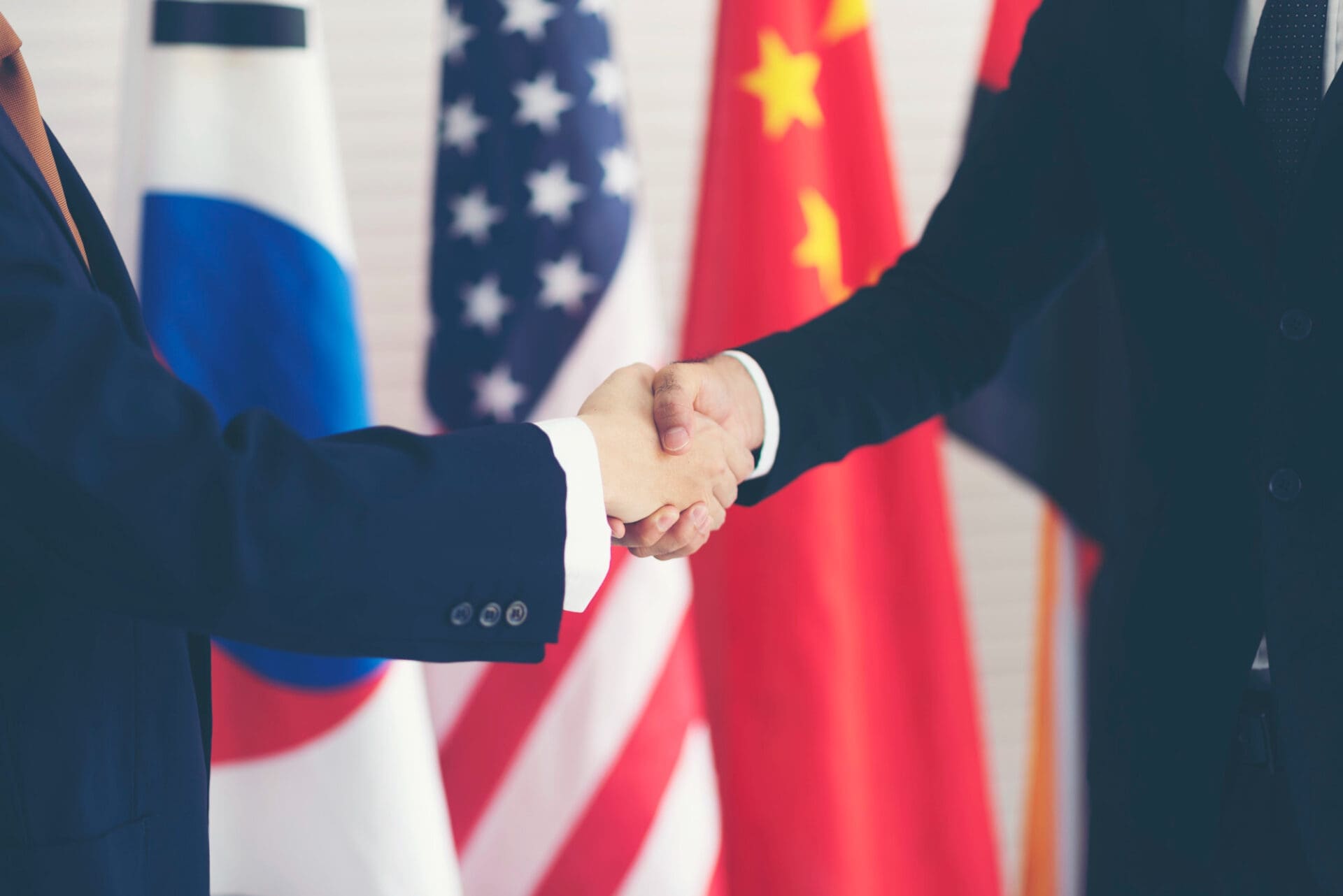 Two diplomats in suits shaking hands in front of Russian, US, and Chinese flags.