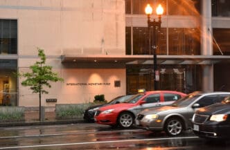 The street-level entrance to the International Monetary Fund building in Washington, DC, with motion-blurred cars on a wet road.