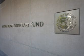 The words "INTERNATIONAL MONETARY FUND" in metal lettering on a beige stone wall next to the silver IMF seal plaque.
