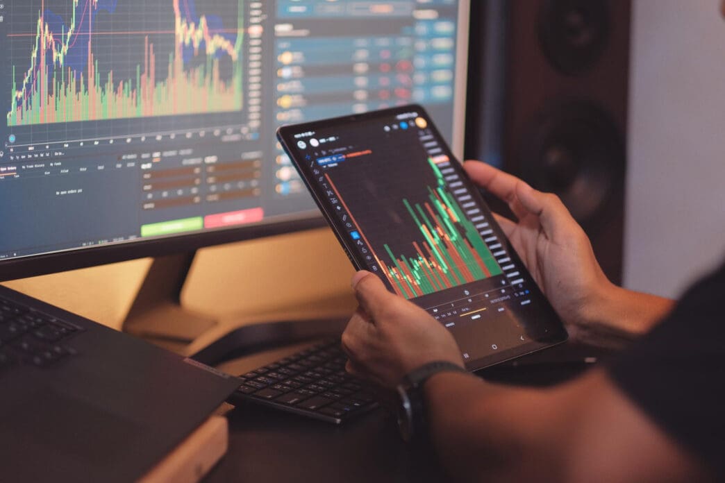 Person analyzing stock market charts on a tablet and computer screens.