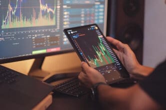 Person analyzing stock market charts on a tablet and computer screens.