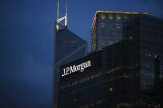 The "J.P. Morgan" logo illuminated in white on a dark corporate skyscraper in Hong Kong at twilight, with the Bank of China Tower visible behind it.