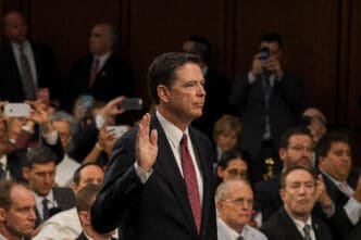 James Comey, in a dark suit, raising his right hand to be sworn in before the Senate Intelligence Committee