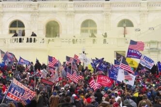 Crowd of Trump supporters with flags gathered near the U.S. Capitol building's exterior with smoke visible.