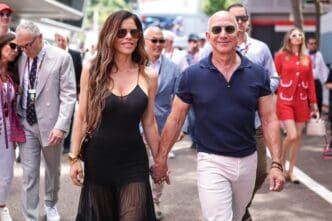 Jeff Bezos and Lauren Sanchez, holding hands, walk through the crowded pit lane at the Monaco F1 Grand Prix