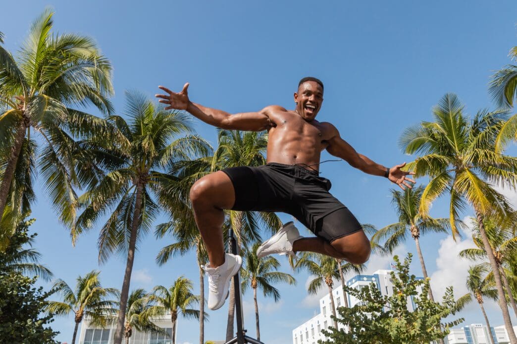 Excited shirtless man in black shorts jumps in the air on a sunny day in Miami Beach