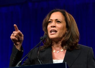 Kamala Harris speaking at a podium, looking up and to the left while emphatically pointing her finger upward