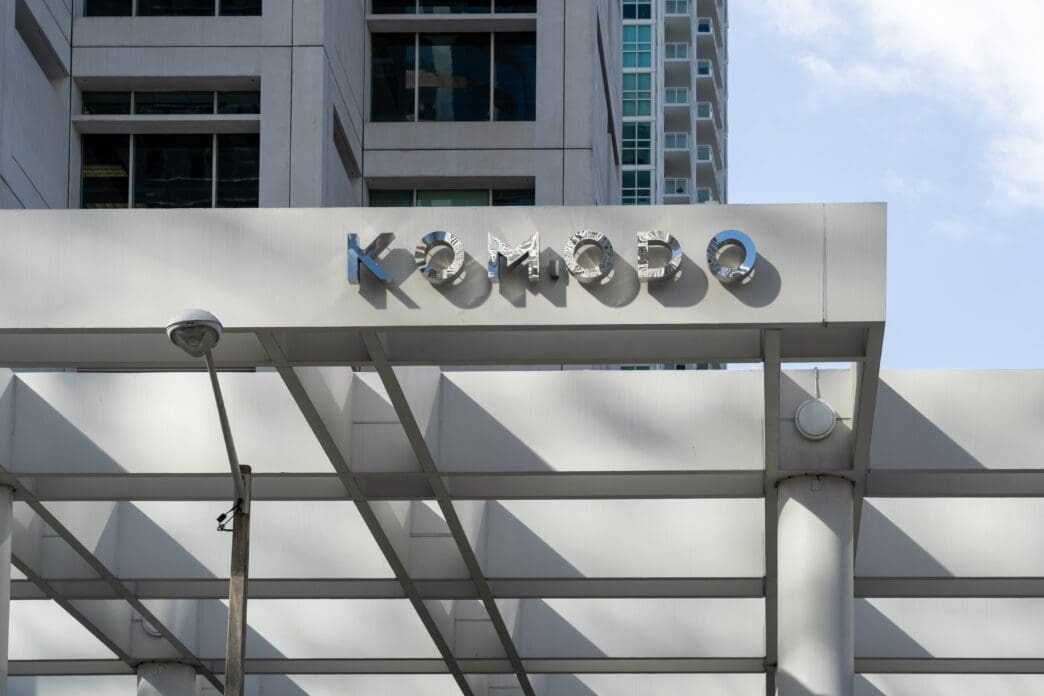 The modern, metallic "KOMODO" sign is mounted on the white facade of a building in Miami, with strong architectural lines below.