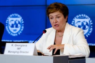 Kristalina Georgieva, IMF Managing Director, speaking at a news conference, wearing a white blazer, with her nameplate visible.