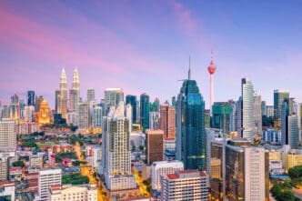 The Kuala Lumpur, Malaysia skyline at sunset, featuring the illuminated Petronas Twin Towers and the KL Tower against a vibrant sky.